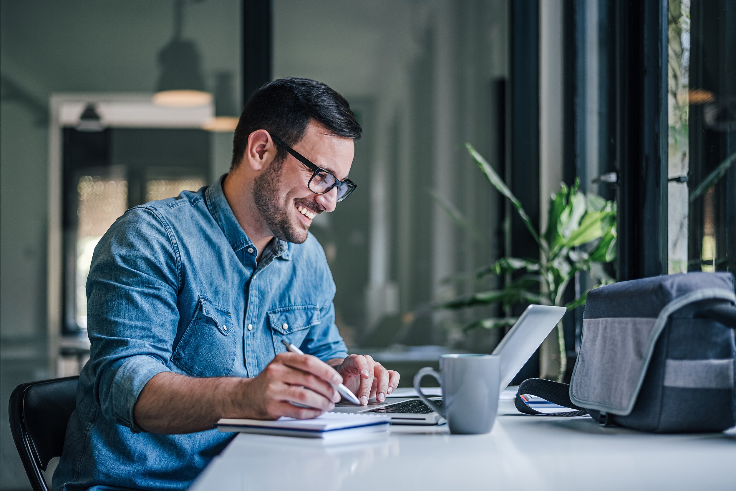 Man-Laptop-Writing-Smiling-AdobeStock_497427933